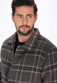 Grau kariertes Wolljackett mit roten und schwarzen Linien, mit einer durchgeknöpften Vorderseite und einem spitzen Kragen, strukturiertem Stoff und legerer Passform.