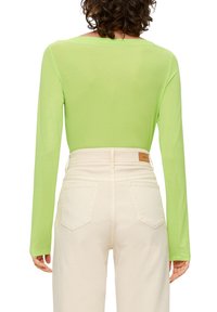 Langdurige, fitted top van neon groene stof, gecombineerd met hoogwaist, lichtbeige broek met achterzakken en een leren label.