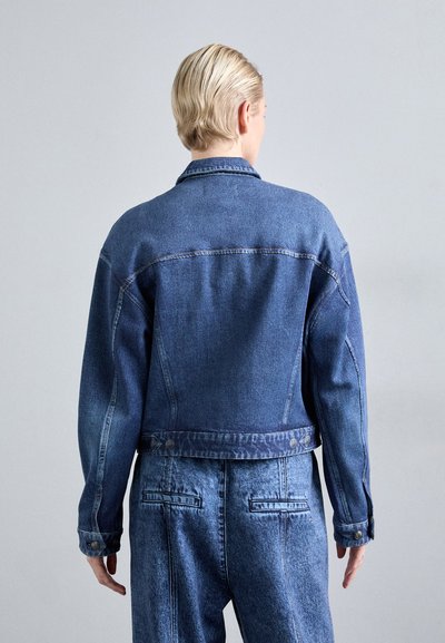 Jachetă din denim cu o formă ajustată, culoare albastru închis, închidere cu nasturi și detalii de cusătură contrastante; asociată cu pantaloni din denim albastru închis asortați.