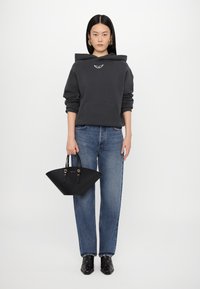 Grijze hoodie met een voorzak, blauwe wijde jeans, zwarte gestructureerde handtas met gouden accenten, en zwarte enkellaarsjes met zilveren studs.