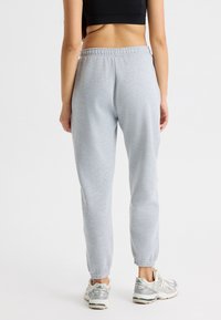 Pantalones de chándal gris claro con cintura y puños elásticos, fabricados en material suave, combinados con zapatillas deportivas grises y blancas.