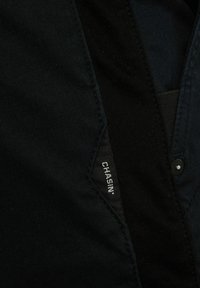 Camisa negra de botones con una etiqueta tejida que dice "Chasin'" en el lateral. La tela parece suave con una textura sutil.