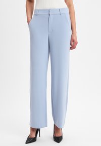 Lichtblauwe broek met wijde pijpen, gemaakt van een zachte stof met voorzakken en een nette afwerking. Gecombineerd met zwarte hoge hakken.