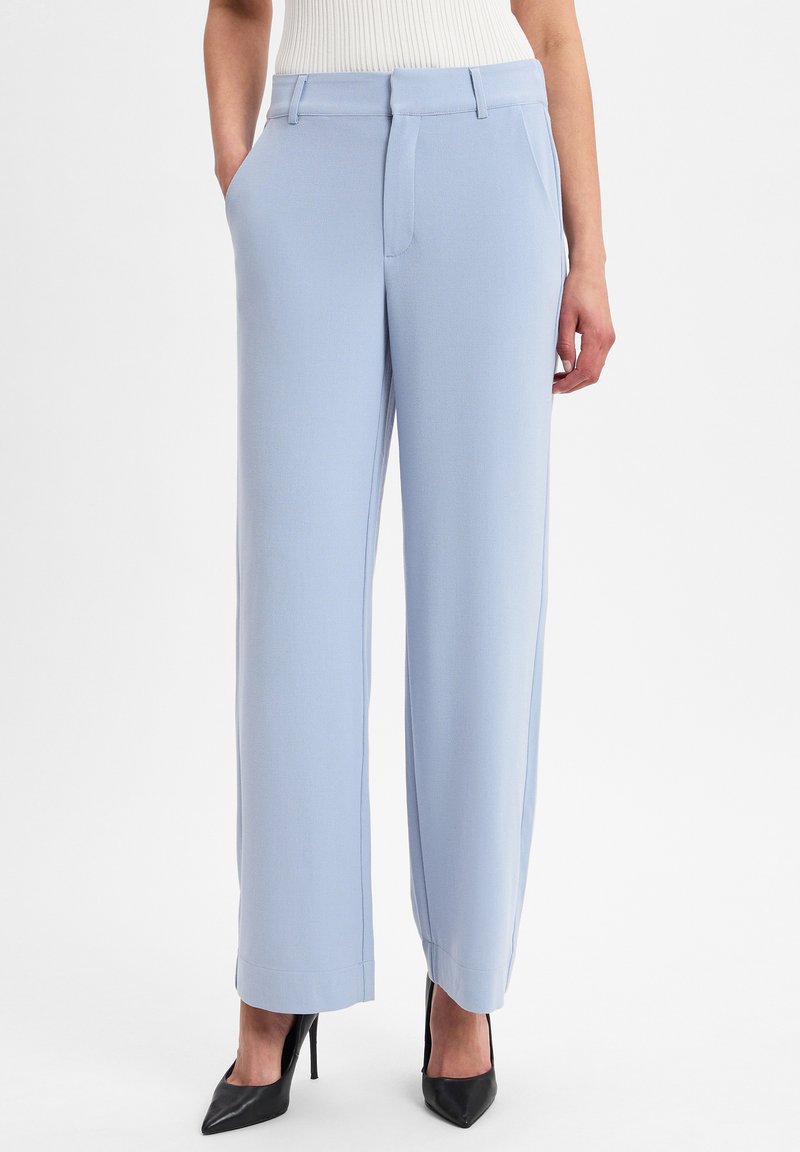 Lichtblauwe broek met wijde pijpen, gemaakt van een zachte stof met voorzakken en een nette afwerking. Gecombineerd met zwarte hoge hakken.