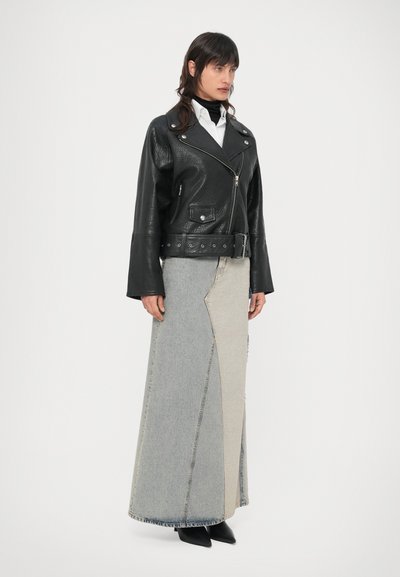 Casaco de couro preto estilo motociclista com lapelas, combinado com uma saia longa de ganga em retalhos, em tons claros e escuros. Sapatos pretos pontiagudos completam o visual.