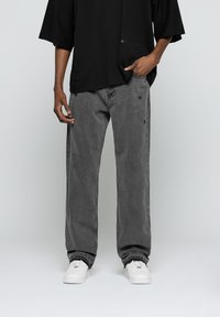 Camiseta negra de gran tamaño con mangas cortas, combinada con jeans rectos grises con ligeros desgastes, complementados con zapatillas blancas.