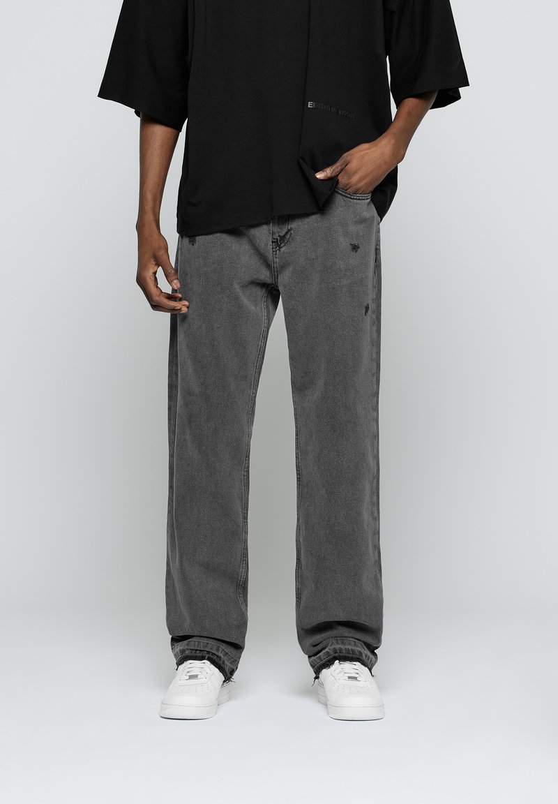 Camiseta negra de gran tamaño con mangas cortas, combinada con jeans rectos grises con ligeros desgastes, complementados con zapatillas blancas.