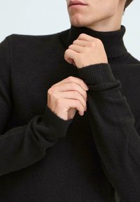 Črna turtlenecka iz soft in teksturiranega materiala. Ima prilegajoče manšete in visok, tesen ovratnik.