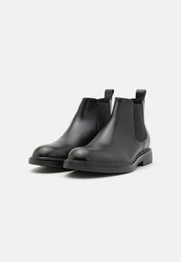 Botas Chelsea de cuero negro con paneles laterales elásticos, punteras redondeadas y lengüetas. Suelas planas de goma que mejoran la durabilidad y la estabilidad.