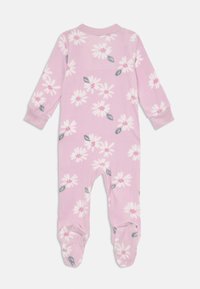 Vaaleanpunainen fleece-haalari, jossa on kukkakuosi, joka sisältää valkoisia päiväkakkaroita ja vihreitä lehtiä. Mukana pitkät hihat ja jalkapohjat, jotka tarjoavat lämpöä.