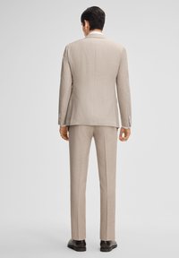 Helle beiger Anzug mit strukturiertem Stoff. Verfügt über einen mittigen Schlitz, einen Reverskragen und schmal geschnittene Hosen. Die Rückansicht zeigt minimale Details.