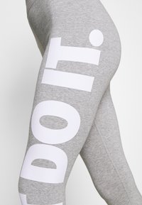 Grå träningsleggings tillverkade av en bomullsblandning med stor vit text som säger "GÖR DET" längs sidan. Slät textur med en åtsittande design.