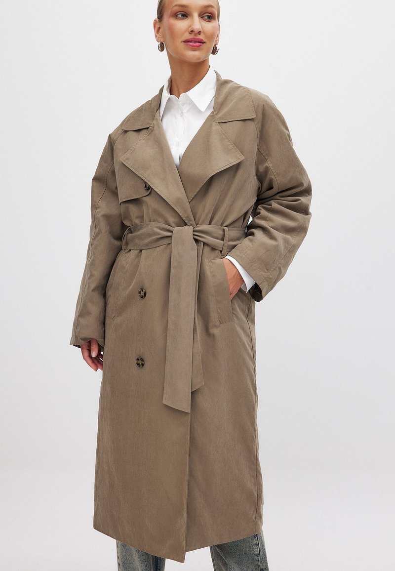 Khaki trench coat s opaskou, dvojradovým zapínaním, veľkými klopami a bočnými vreckami. Vyrobený z hladkej, textúrovej tkaniny.