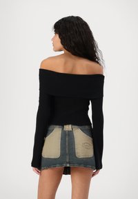 Svart ribbet av-shoulder topp kombinert med en denim mini-skjørt med kontrasterende brune lommer og en falmet blå nyanse.