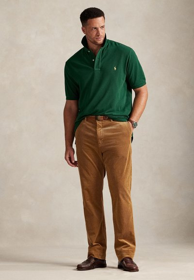 Πράσινο βαμβακερό πουκάμισο πόλο με διπλωμένο γιακά, συνδυασμένο με παντελόνι από κοτλέ σε ταμπά απόχρωση με διακριτικές κάθετες ρίγες και καφέ δερμάτινα παπούτσια.