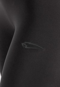 Zwarte sportlegging van soepel, rekbaar materiaal met een subtiel zwart logo op de dij, ontworpen voor comfort en flexibiliteit.