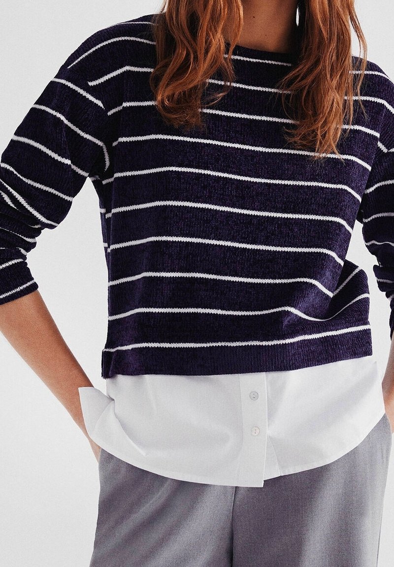Navy and white striped knit sweater with a wide neckline and long sleeves, layered over a white button-up shirt tucked into gray trousers.