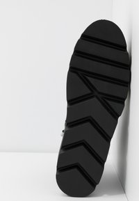 Suela de zapato de goma negra con un patrón de relieve en zigzag, que presenta líneas de agarre texturizadas y una zona de puntera redondeada.