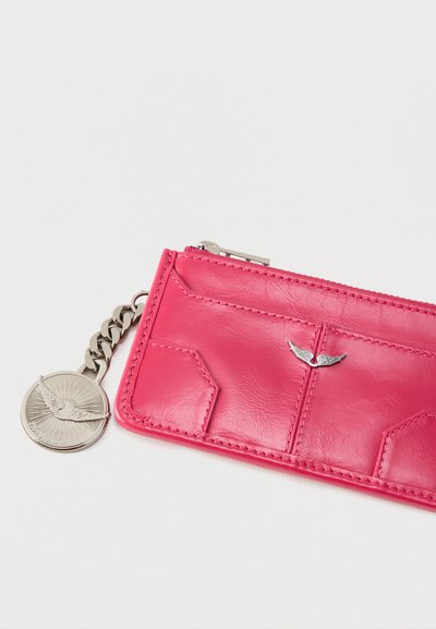 Μικρό ορθογώνιο ροζ δερμάτινο πορτοφολάκι με φερμουάρ, ασημί έμβλημα με φτερά μπροστά και προσαρτημένη ασημένια αλυσίδα με κυκλικό μενταγιόν με φτερά.