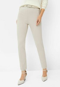 Beige maßgeschneiderte Hosen mit schlanker Passform, mit seitlichen Taschen und einem passenden Gürtel. Kombiniert mit cremefarbenen Riemchen-Stilettos.