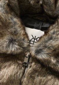 Könnyű műszőrméből készült gallér, különböző barna árnyalatokban, sima tapintással. Fém cipzárral és logóval díszített fekete béléssel rendelkezik.