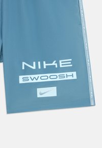 Calções atléticos azuis feitos de um tecido suave. Apresentam grandes logótipos "NIKE" e "SWOOSH" em branco, com um painel lateral estampado.