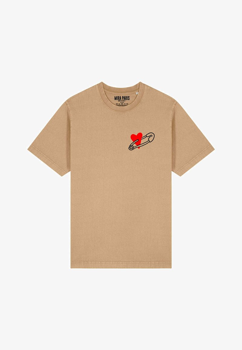 La t-shirt in cotone beige presenta maniche corte, un col rotondo e una grafica di una spilla di sicurezza nera con un cuore rosso sul lato sinistro del petto.
