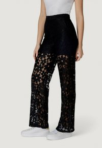 I pantaloni neri in pizzo presentano un motivo floreale con un design semitrasparente. La forma a gamba larga contrasta con un cinturino nero opaco.