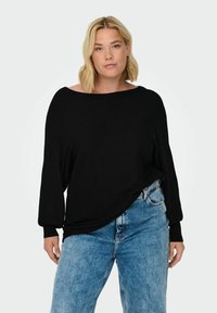 Black oversized ribbed sweater with wide boat neckline and long, fitted sleeves, paired with high-waisted light blue denim jeans.