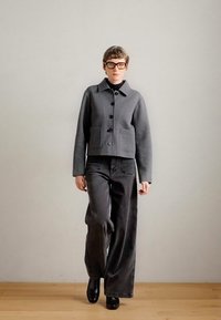 Casaco cinza em mistura de lã com colarinho e bolsos frontais, emparelhado com calças negras de perna larga. Footwear é botas pretas com salto arredondado.