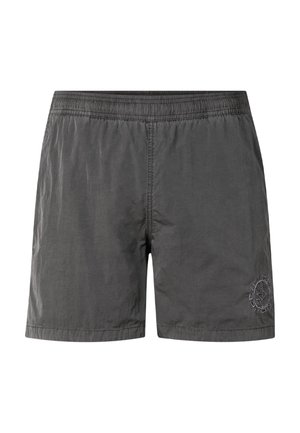 Ung mand med muskuløs bygning iført mørkegrå badeshorts og sorte flip-flops, stående mod en ensfarvet lys baggrund.