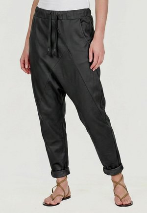Personne portant un pantalon jogger noir taille élastique avec cordon et revers retroussés, associé à des sandales plates marron à brides.