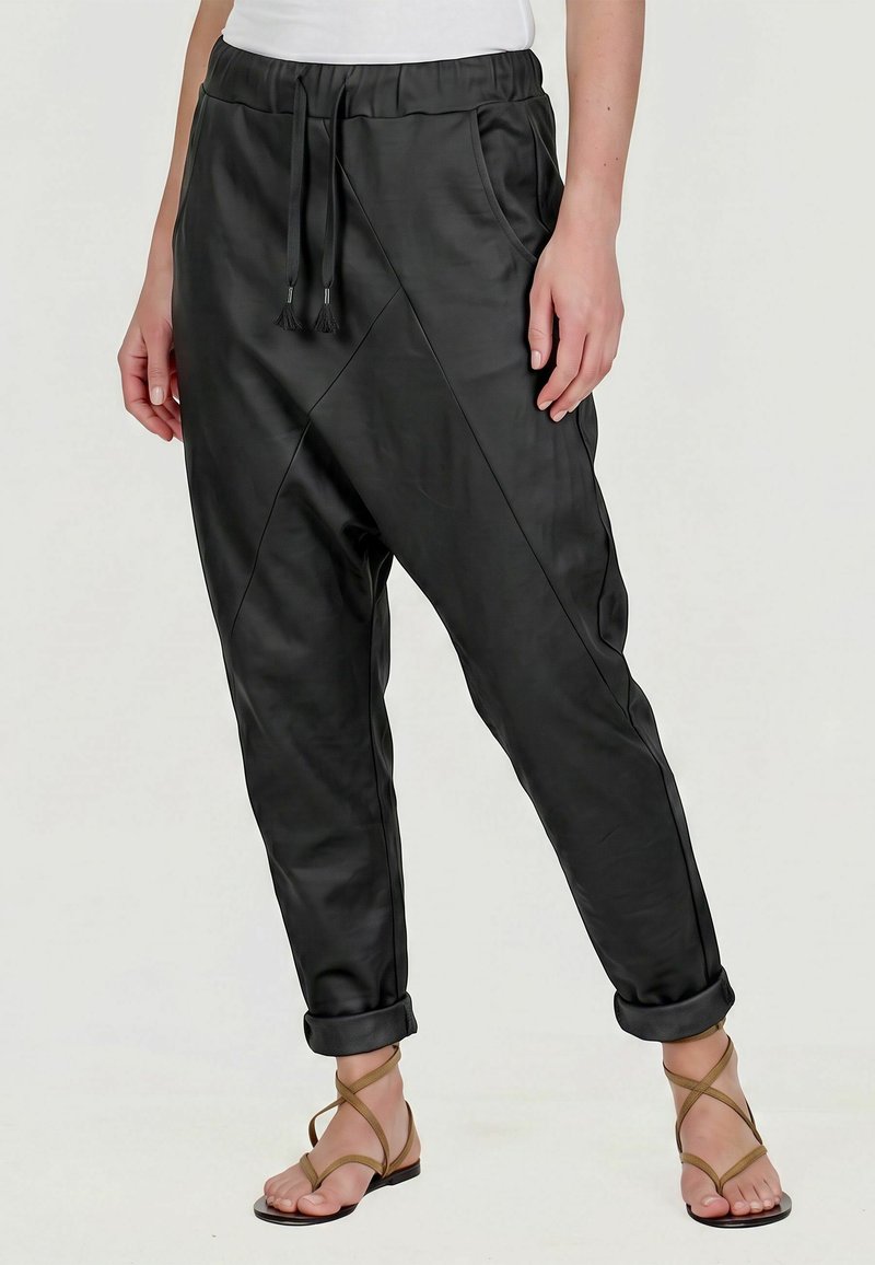 Personne portant un pantalon jogger noir taille élastique avec cordon et revers retroussés, associé à des sandales plates marron à brides.