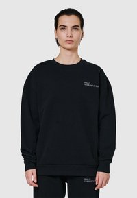 Lös svart sweatshirt i bomull, med rund halsringning och ribbade manschetter. Liten vit textlogo på bröstet som ger detalj.