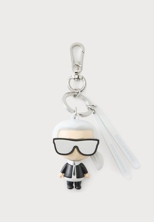 Porte-clés avec une petite figurine portant de grandes lunettes de soleil noires, une veste noire, une chemise blanche, une cravate noire, des cheveux blancs en queue de cheval et deux étiquettes blanches.