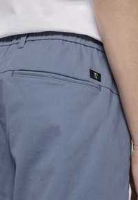Pantalones azul claro con cintura elástica, que cuentan con un bolsillo trasero y una pequeña etiqueta de marca negra. La tela tiene una textura suave.
