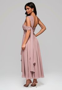 En flödande, off-the-shoulder klänning i rosarosa med en åtsittande bodice och draperade accenter, tillsammans med strappy högklackade sandaler.