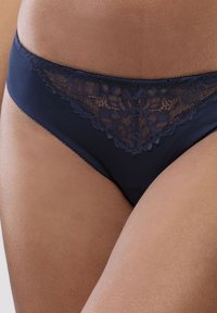 Granatowe figi z koronkowym wykończeniem, wykonane z gładkiego materiału. Koronka ma kwiatowy wzór wzdłuż pasa i wycięć na nogi.