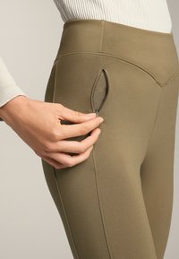 Olivazöld leggings, letisztult dizájnnal, oldalt egy kis cipzáros zsebbel. Simább, rugalmas anyagból készültek.