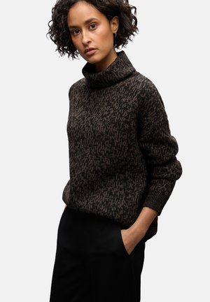 Brązowy sweter z wzorem w sploty, z golfem, o luźnym kroju, z prążkowanymi mankietami i lekką teksturą, zestawiony z czarnymi spodniami.
