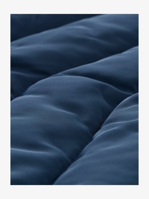 Tuvplāns gludai tumši zilai izšūtai auduma daļai ar mīkstu, apaļu dūrienu, veidojot polsterētas, izceltas sekcijas.