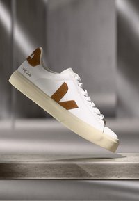 Sneaker bianco con accentuazioni marroni, dotato di una suola texturizzata, design con lacci e branding "VEJA" sui lati e sul tallone.