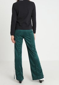 Top nero a maniche lunghe con scollatura rotonda, abbinato a pantaloni larghi verde satinati con strisce bianche laterali e spacchi.