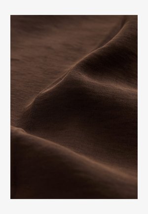 Tissu brun texturé, présentant des ondulations douces et un éclat subtil. Le matériau semble doux, léger et finement tissé.