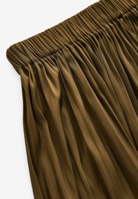 Gonna plissee marrone con vita elastica, realizzata in tessuto leggero, con pieghe verticali per texture e fluidità.