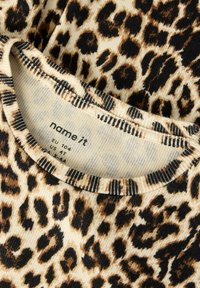 Marškiniai su leopardų raštu, riboto audinio, šviesios kreminės spalvos pagrindas, juodi ir rudi dėmės, ir dryžuotas apykaklės kraštas. Etiketė matoma viduje apykaklės.