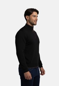 Suéter ligero negro con un alto cuello, cremallera de cuarto y puños acanalados. Presenta un acabado en contraste en el dobladillo. Fabricado con una tela suave.