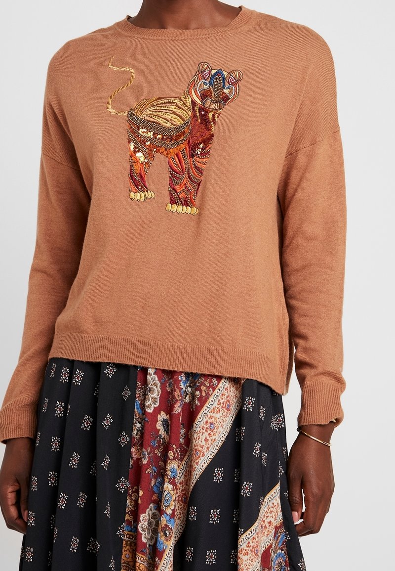 Pull en maille marron avec un motif de lion coloré brodé. Le lion présente des motifs et des textures complexes, créant un élément visuel vibrant.