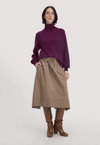 Lila Rollkragensweater, beige knöchellange Rock mit elastischem Bund, braune kniehohe Stiefel, schlichter Hintergrund.