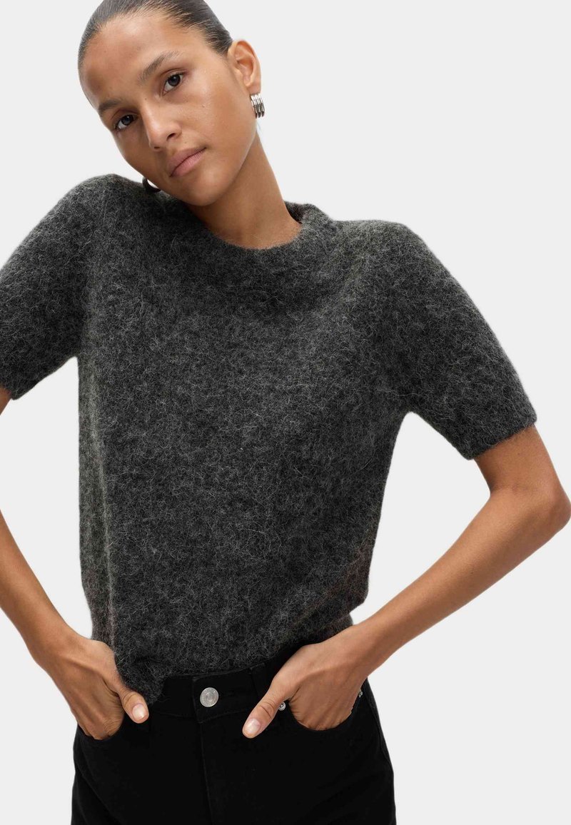 Maglione a maniche corte di colore grigio scuro, realizzato in un materiale morbido e peloso, con scollatura rotonda. Abbinato a pantaloni neri a vita alta con un bottone argentato.